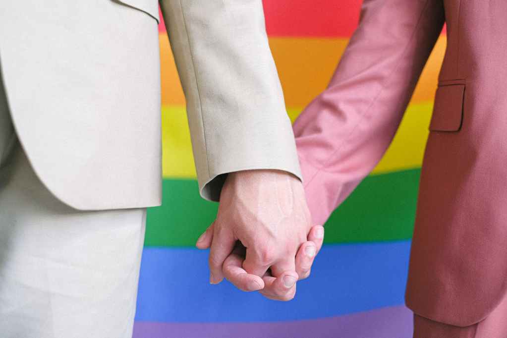 couple holding hands in front of a gay pride flag