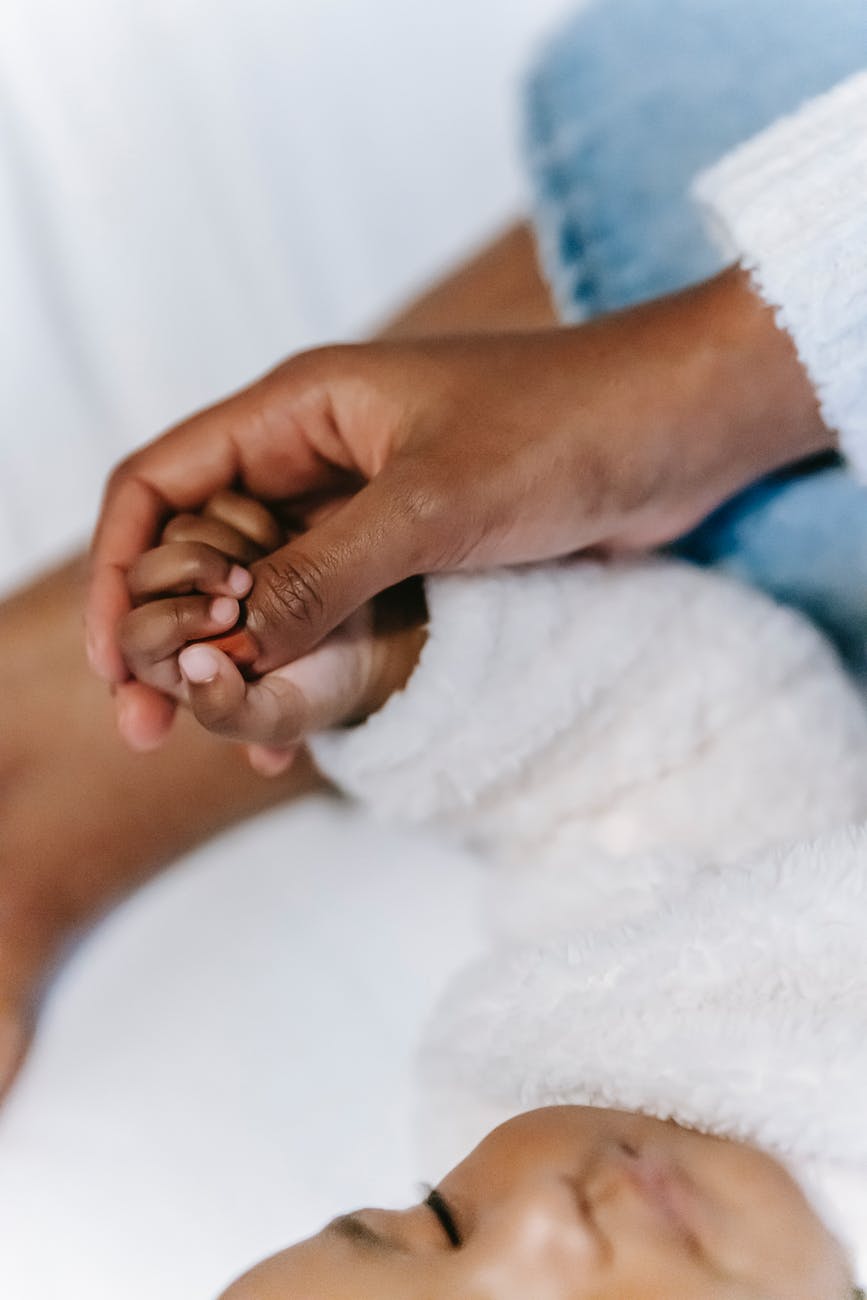 anonymous ethnic woman touching hand of sleeping baby on bed