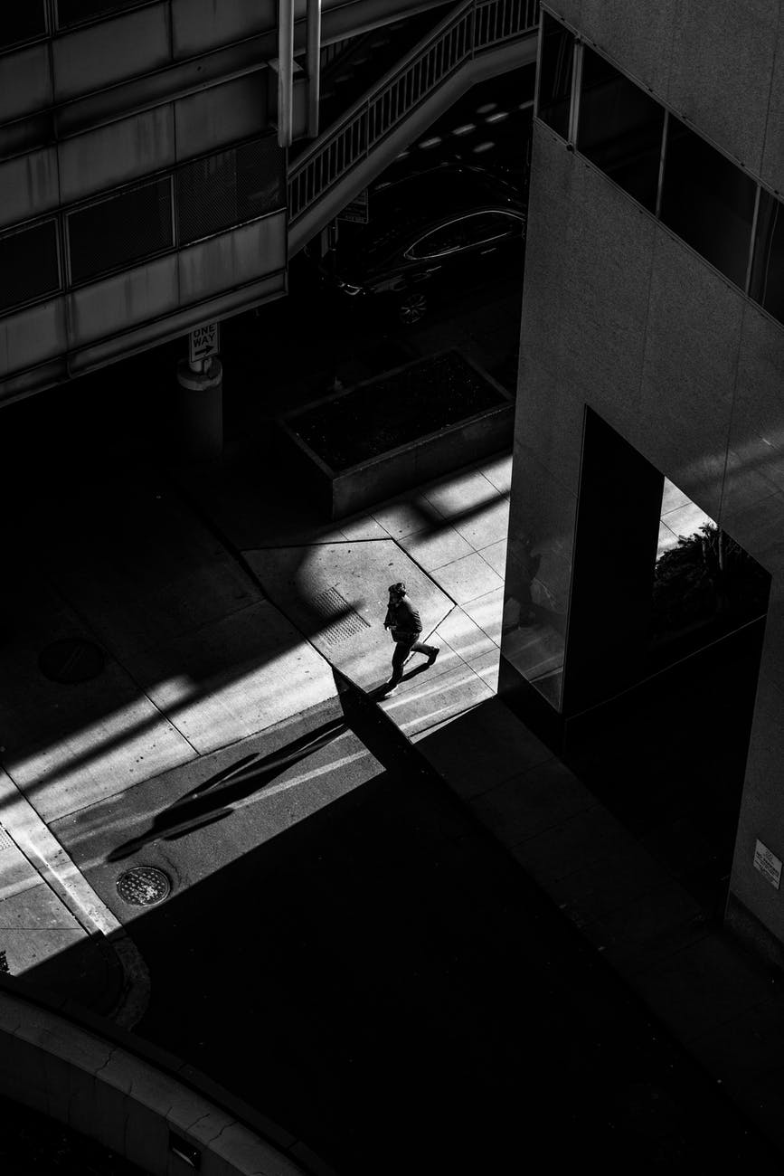 grayscale photo of man walking on street near buildings
